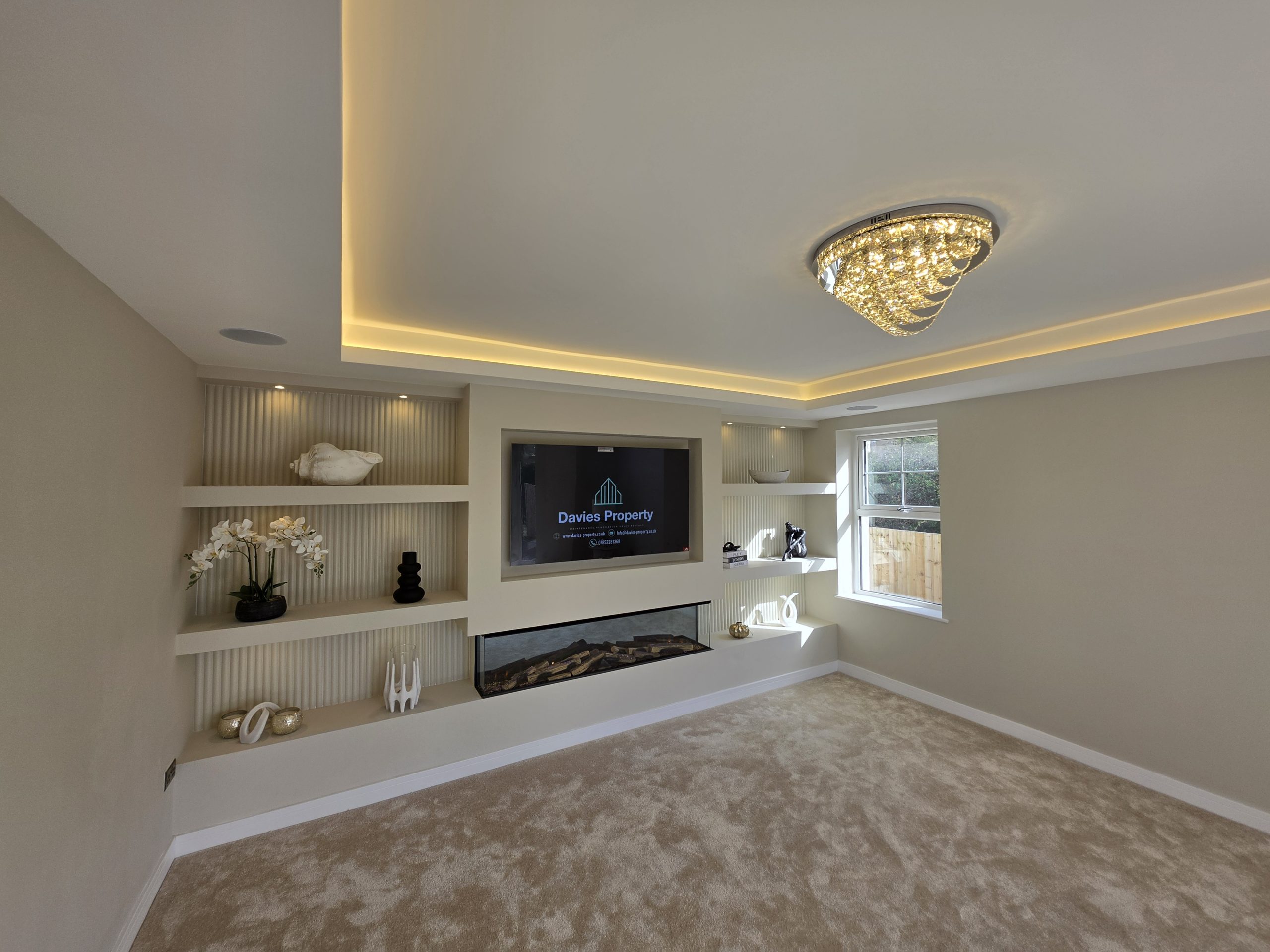 Luxury living room with a bespoke media wall, electric fire, dropped ceiling with integrated LED lighting and crystal chandelier