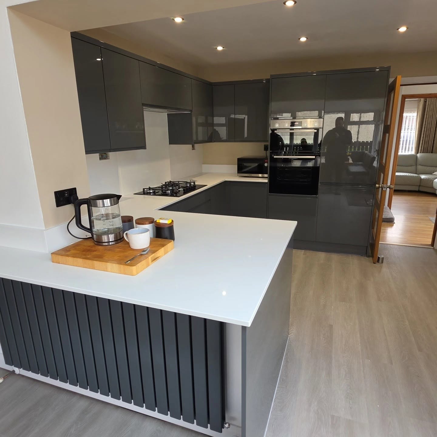 Modern open-plan Wren kitchen after renovation with dark grey gloss units, white worktops and grey oak LVT flooring