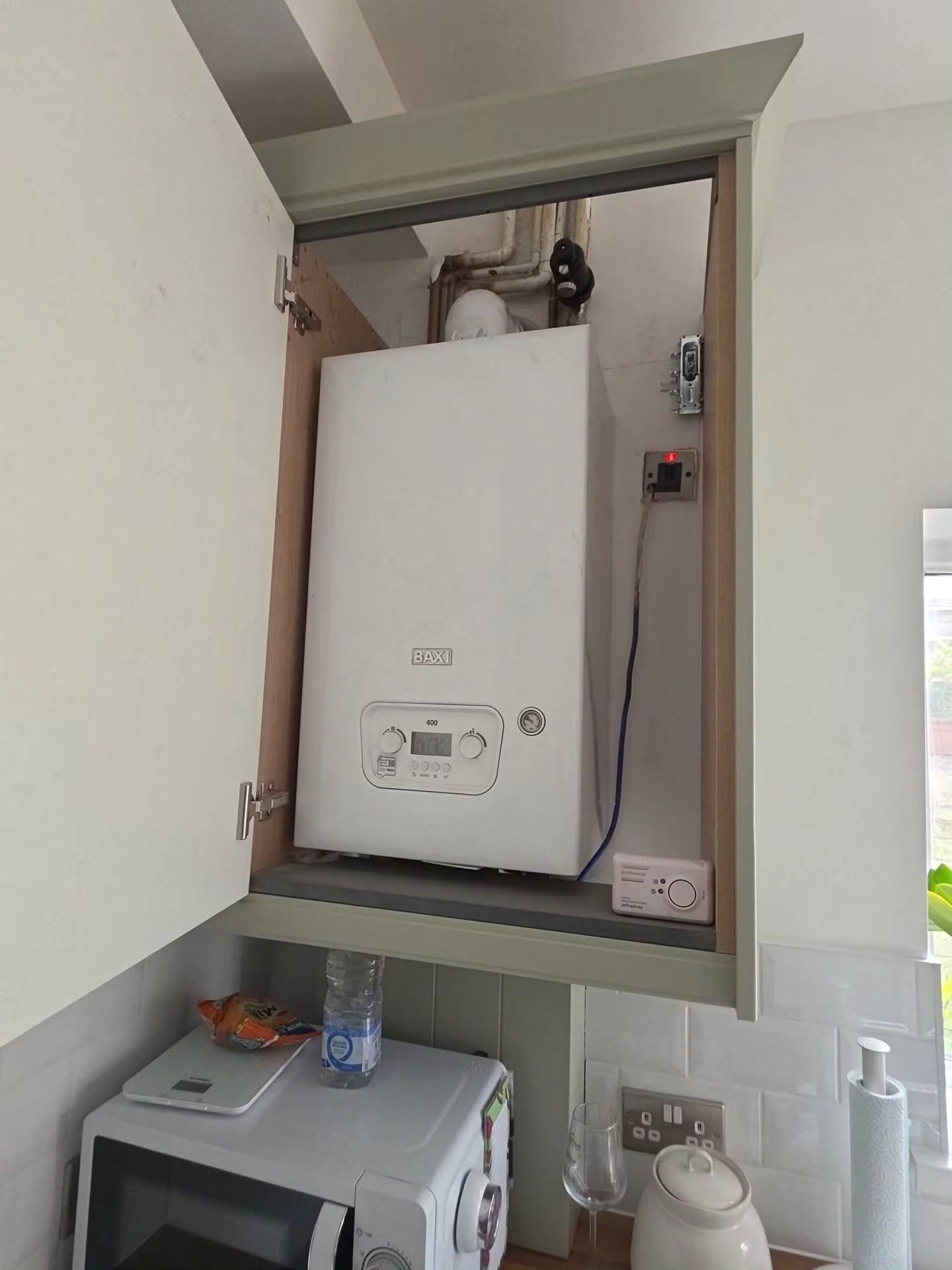 New gas boiler installation neatly concealed within a sage green kitchen wall cabinet