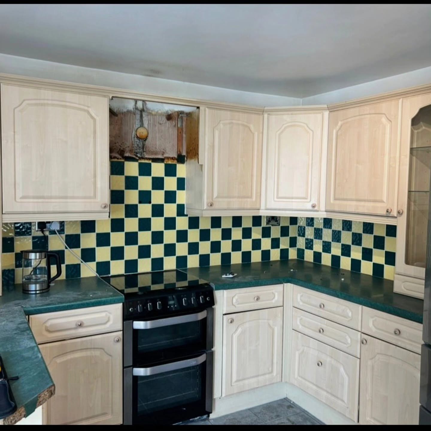 Old kitchen with cream units and green and yellow checkerboard tiles before transformation