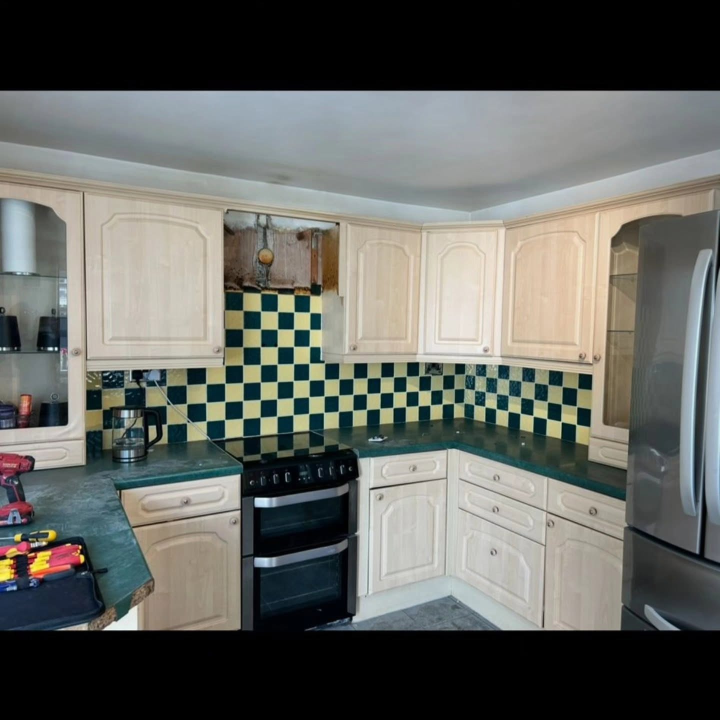 Outdated kitchen with cream cabinets and green checkerboard tiles before renovation