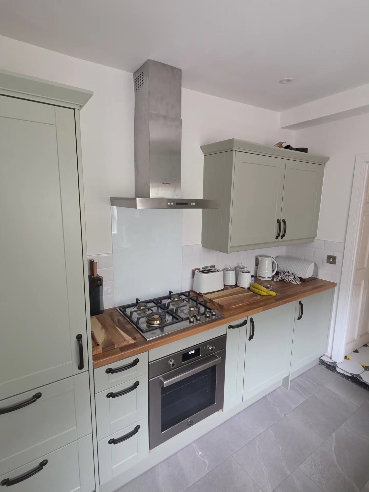 Sage green shaker kitchen with gas hob, integrated oven, oak worktops and grey tiled flooring