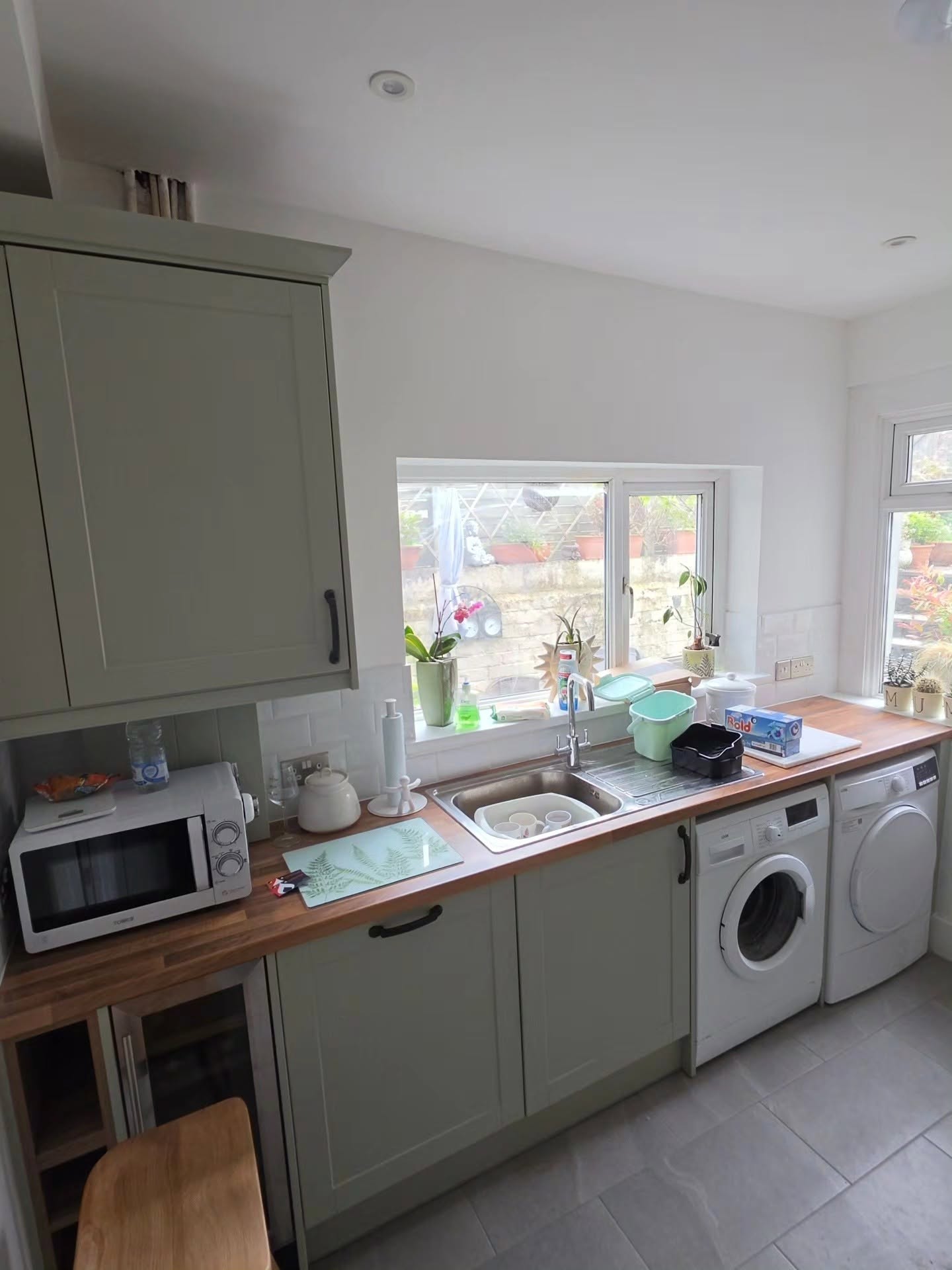 Sage green Wren shaker kitchen with oak worktops and sink beneath the window in the utility area