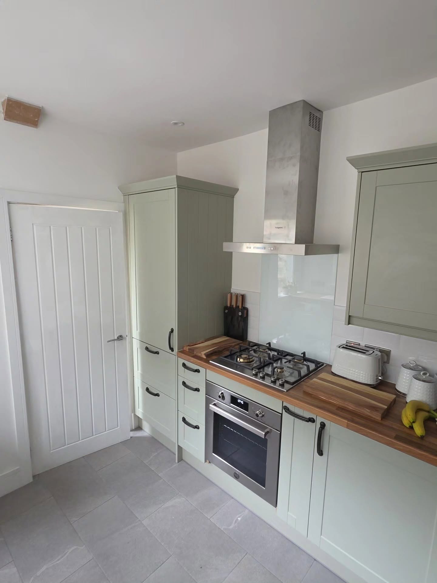 Sage green Wren shaker kitchen with gas hob, chimney extractor, oak worktops and Dordogne internal door