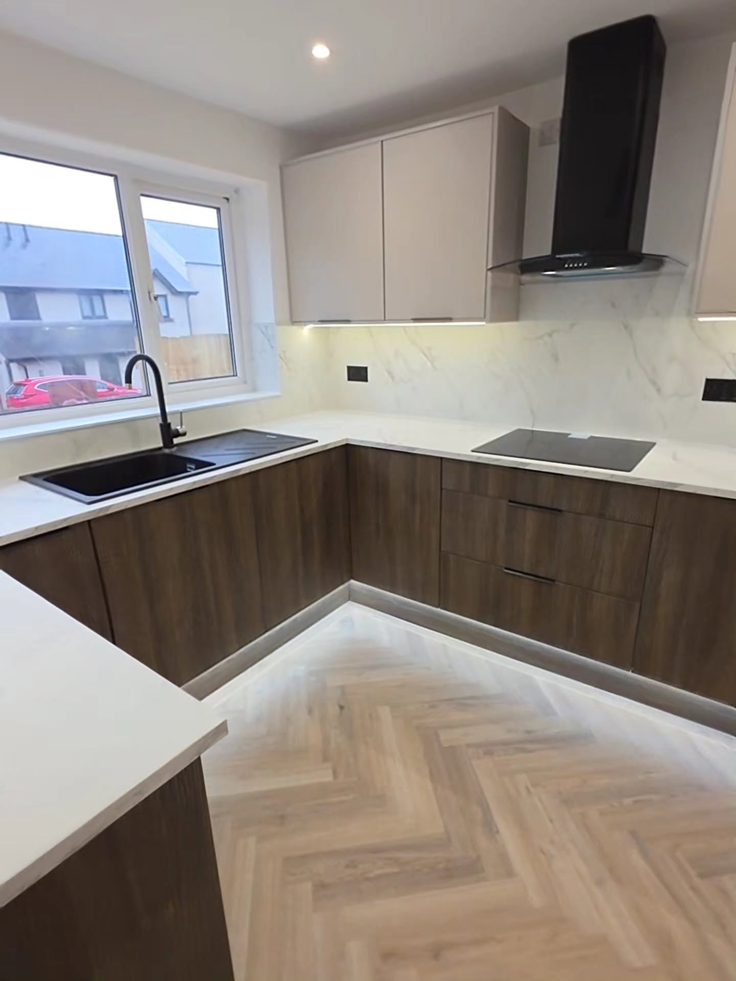 Black chimney extractor above an induction hob with cashmere wall units and marble-effect backboards