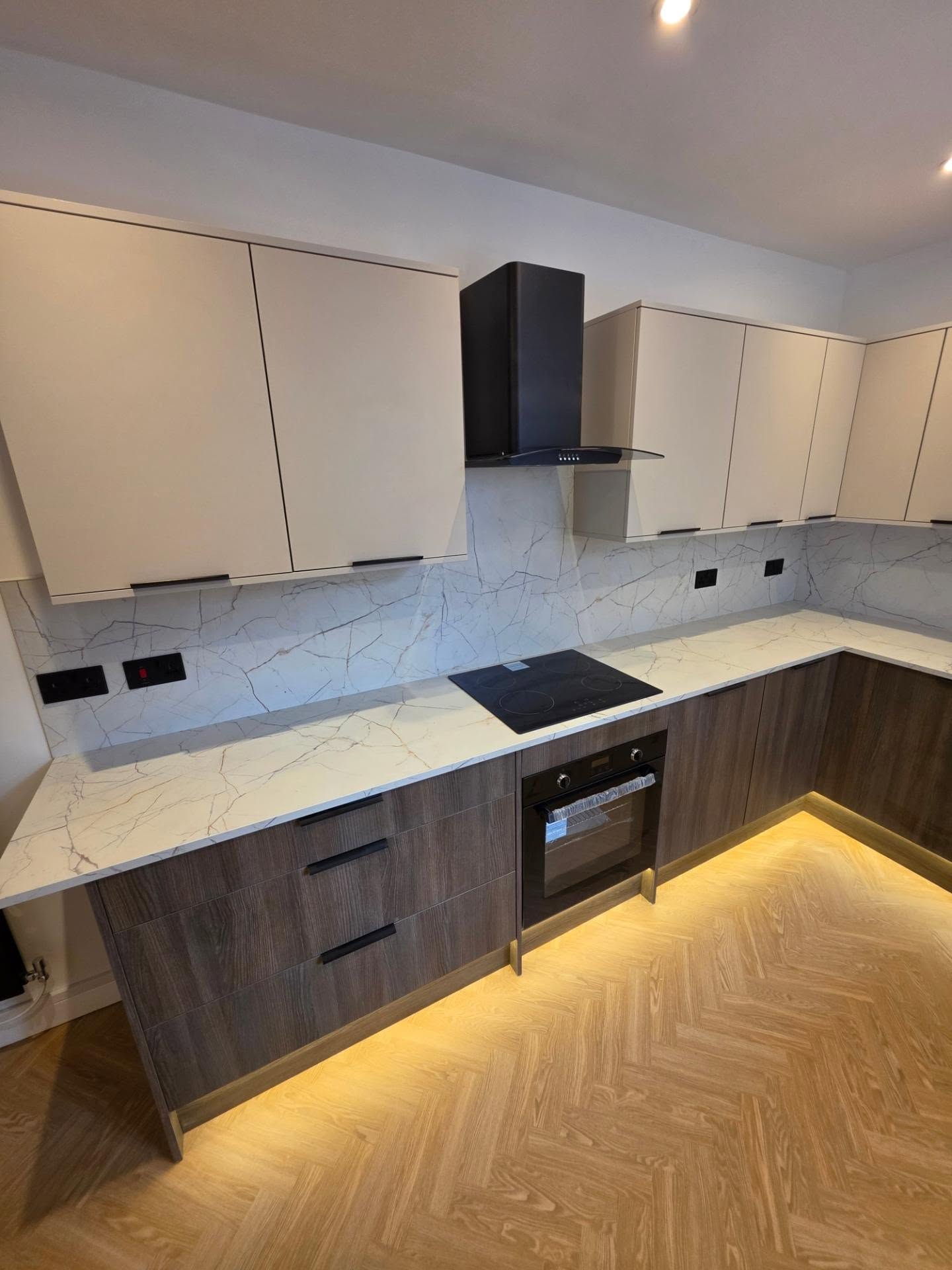 Induction hob beneath a black chimney extractor with cashmere wall units and marble-effect splashback