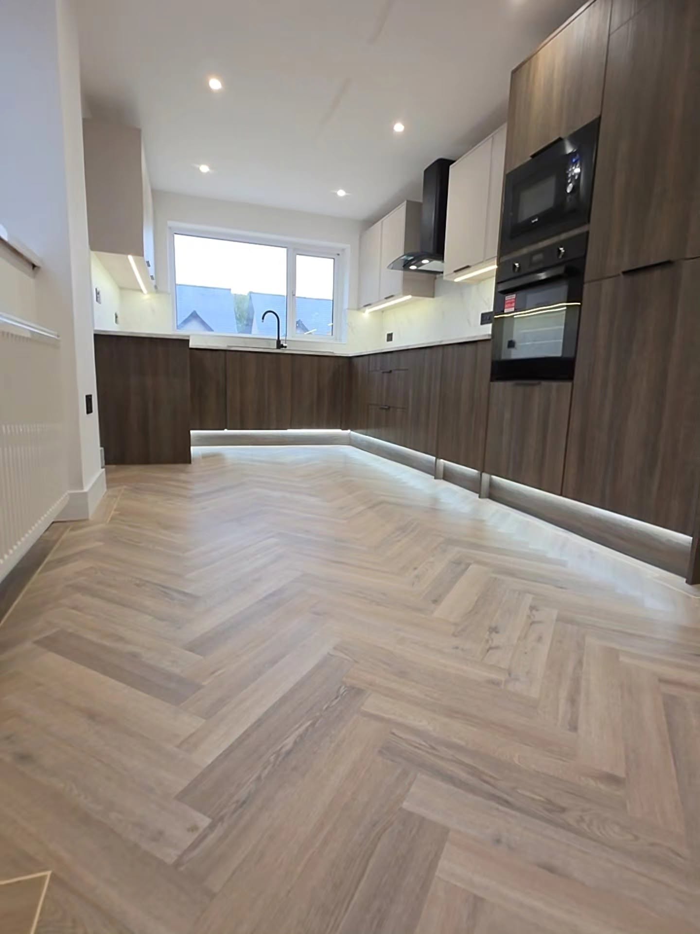 Open-plan two-tone kitchen in Senghenydd with walnut base units, cashmere wall units and herringbone LVT flooring