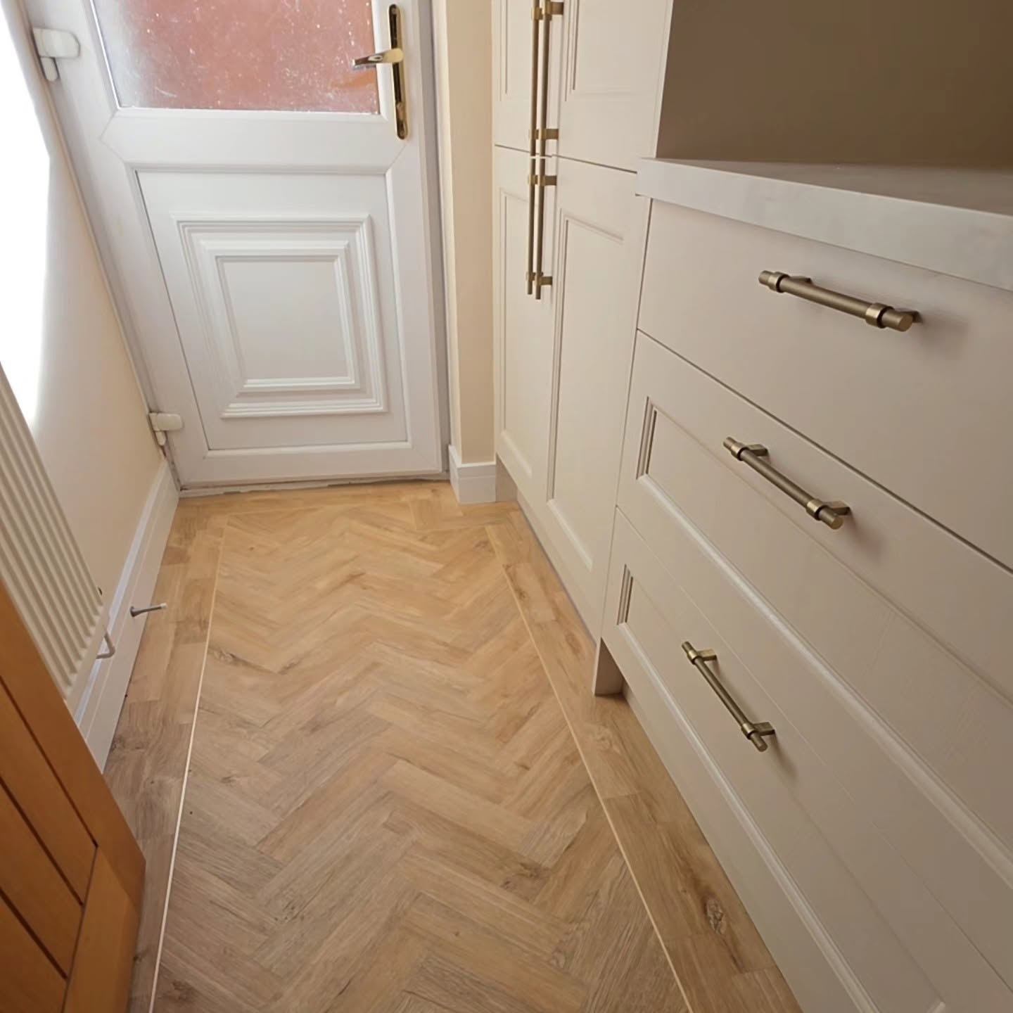 Utility room with herringbone LVT flooring, gold feature-strip border and cream Howdens drawer units with brass handles