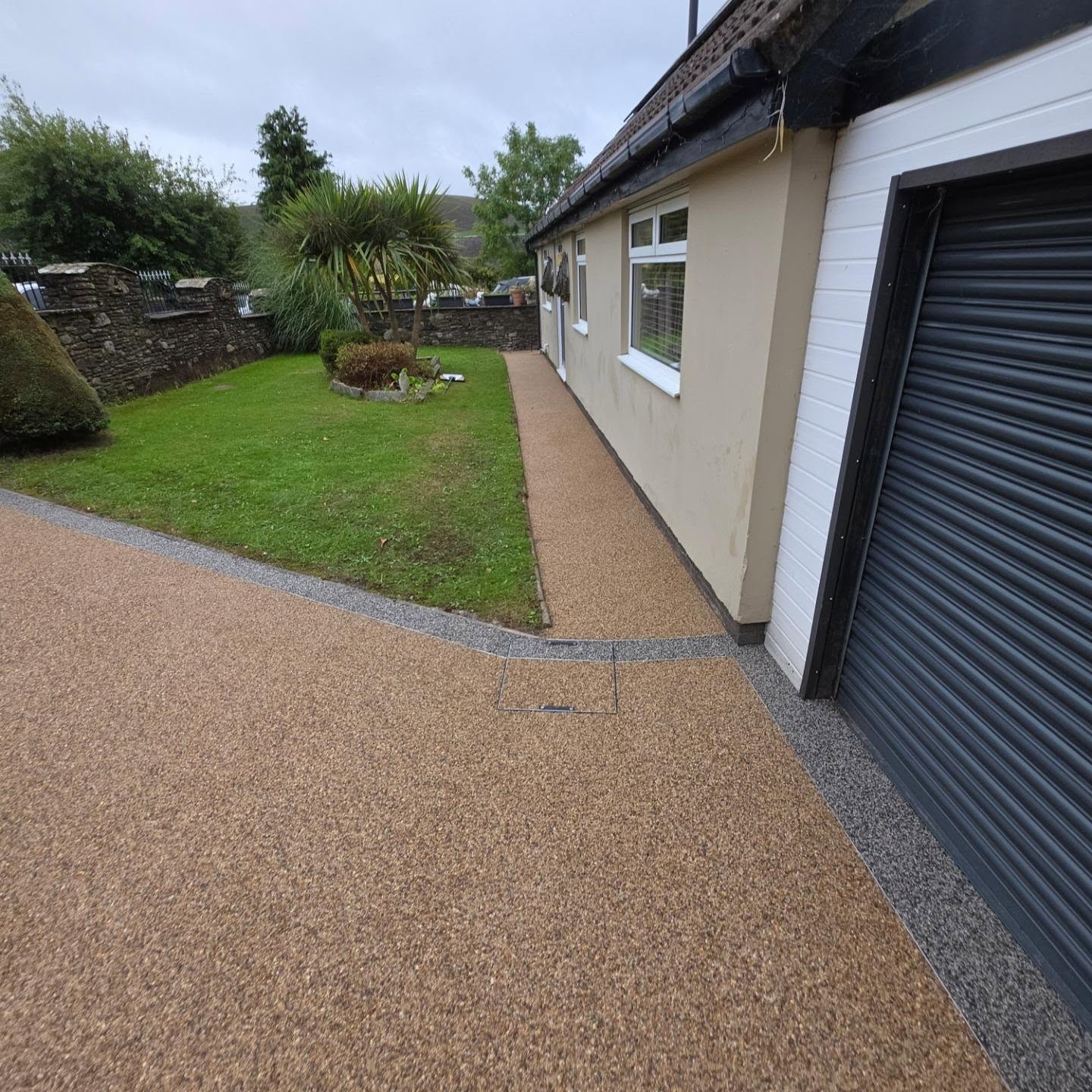 Completed Vuba resin-bound driveway in Kilimanjaro with a contrasting Matterhorn border beside a bungalow and garage