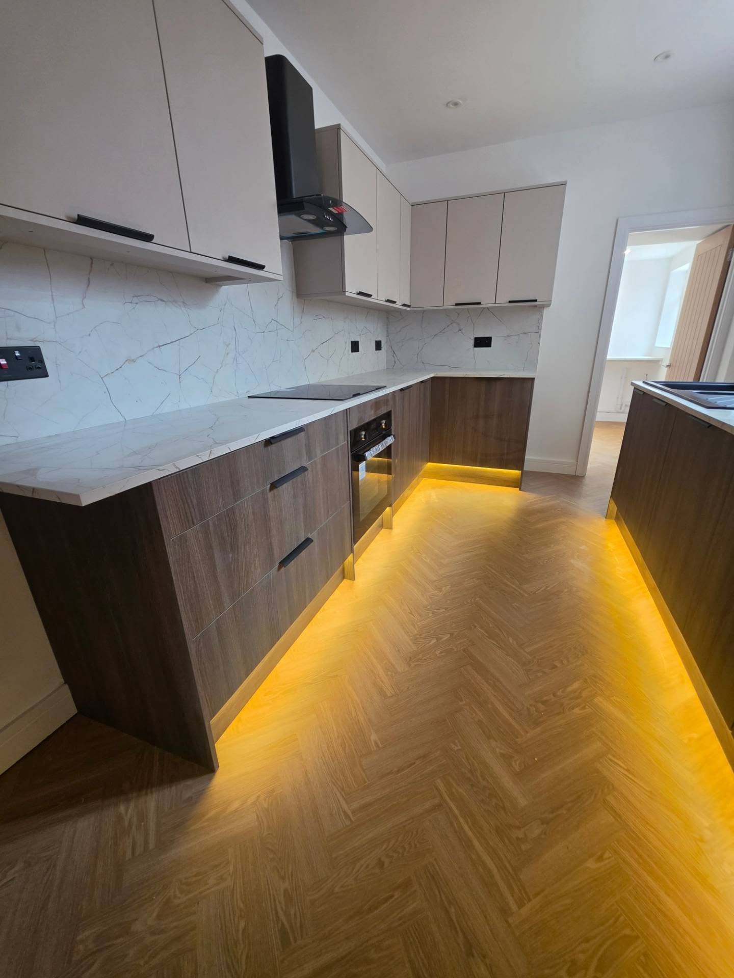 Two-tone walnut and cashmere kitchen in Llanbradach with LED plinth lighting, marble-effect worktops and herringbone flooring