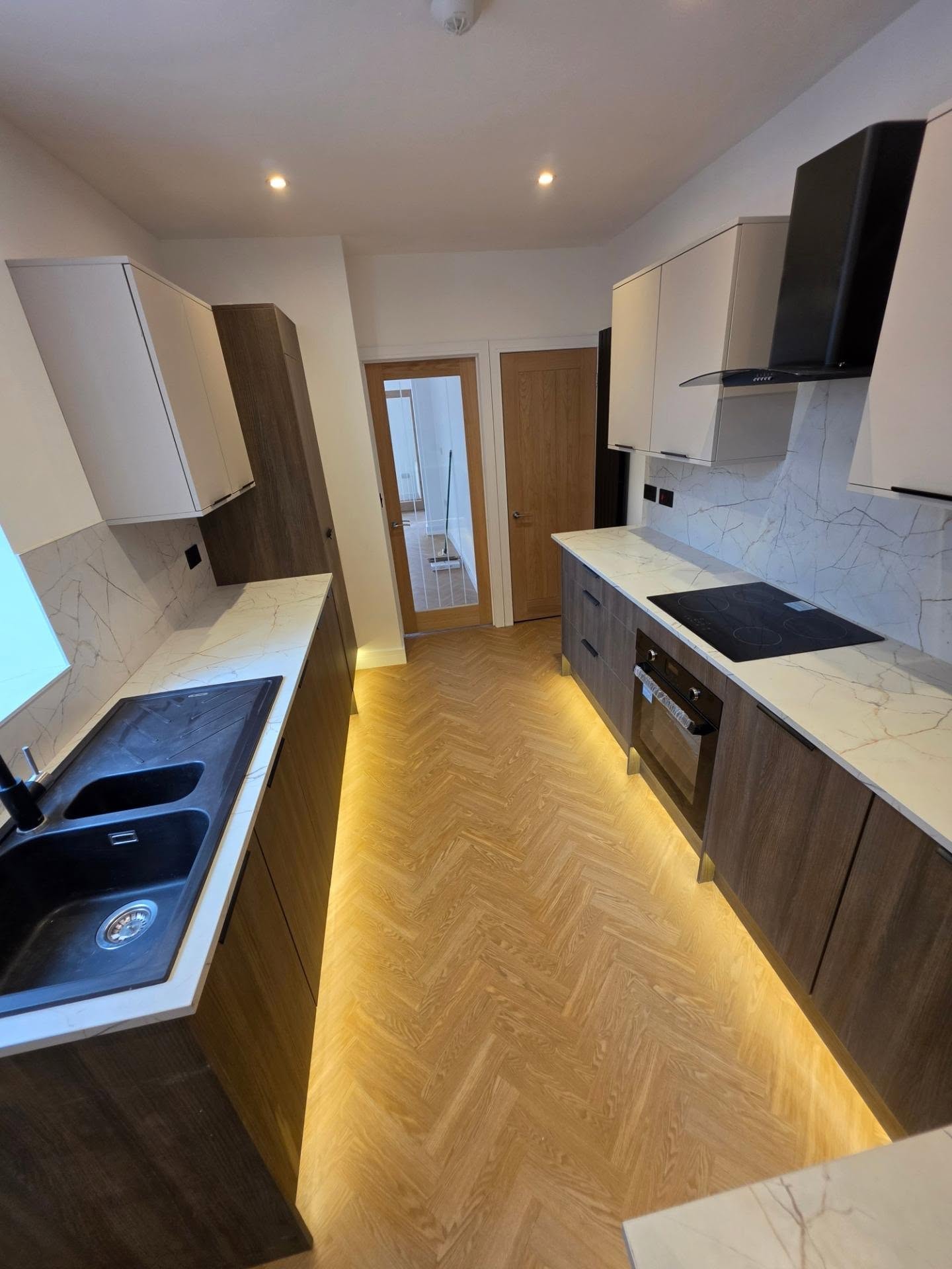 Galley view of the walnut kitchen with integrated oven, black extractor and marble-effect splashback